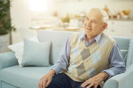 Happy male pensioner sitting on couch in living room while resting at home. Copy space. Lifestyle concept