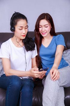 two young woman listening to music in headphones with moblie on sofa at home