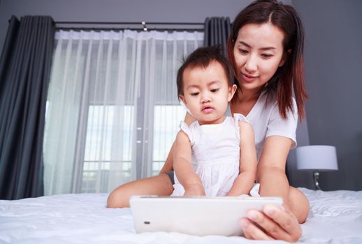 Mother and baby are looking to play and read tablet computer on bed at home