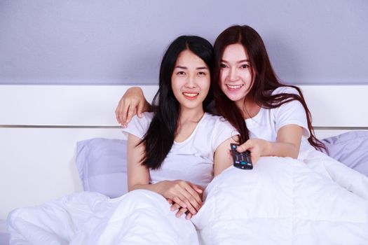 two best friends watching tv with remote on bed in the bedroom