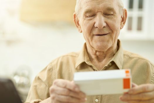 Copy space photo of elderly man looking at a tiny box of medication in his hands