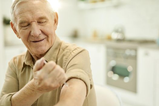 Copy-space photo of a positive aged man performing an arm injection on his arm at home