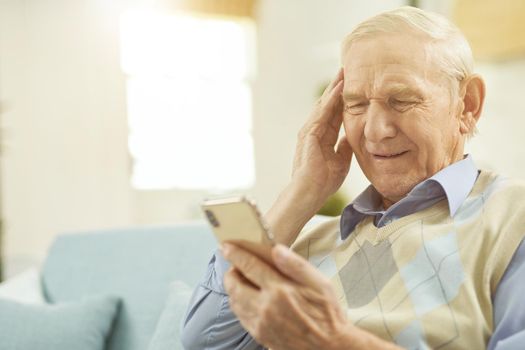 Gray-haired man sitting on the couch and explaining to the doctor that he has headache while using phone