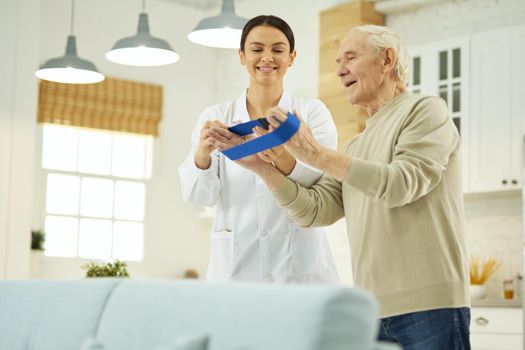 Positive female doctor in a white coat explaining to a pensioner how to do exercises at home