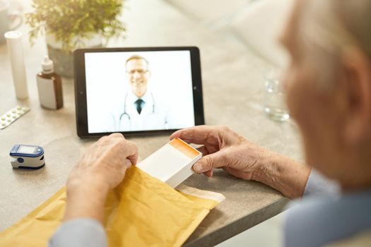 Senior man receiving medciation via mail delivery and video-calling his medical doctor