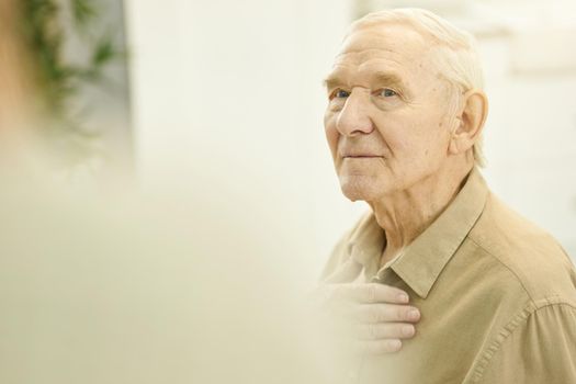 Copy-space photo of a serious-looking senior citizen holding hand on chest