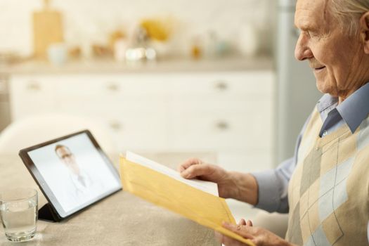 Copy-space photo of an eldelry man holding a yellow parcel while contacting his doctor online