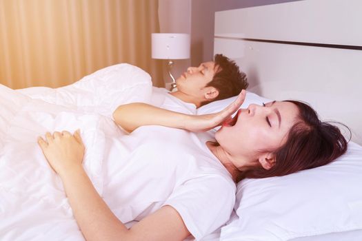 young woman yawning and her husband sleeping on bed