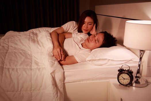 sleeping man lying on bed with woman concerned comforting him at the night