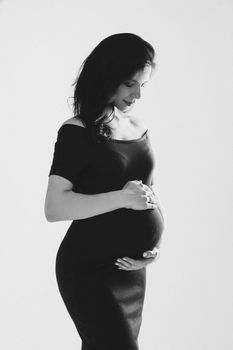 Beautiful young pregnant woman embracing belly posing in studio, black and white photo. Happy pregnancy and motherhood. High quality photo