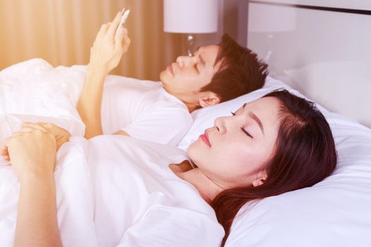 woman in bed with her sleeping and her husband texting on smartphone in the bedroom