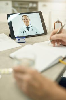 Copy space photo of responsible patient writing while listening to doctor advice on a video-call online consultation