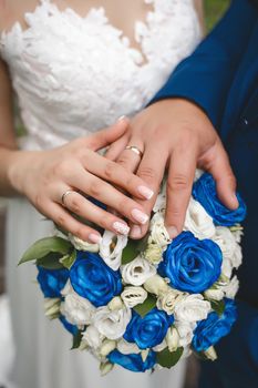 The hand of the bride and groom at the wedding put their hands on a bouquet of flowers roses close up.