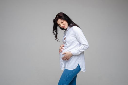 Beautiful female expecting baby, touch pregnant belly feeling pain on gray studio background. Beginning of labor pains. High quality photo