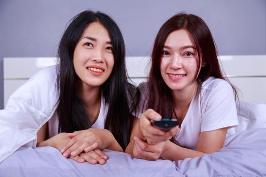 two best friends watching tv with remote on bed in the bedroom