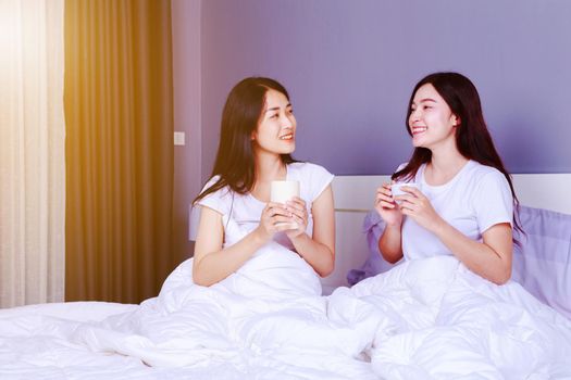 two best friends talking and drinking a cup of coffee on bed in the bedroom 