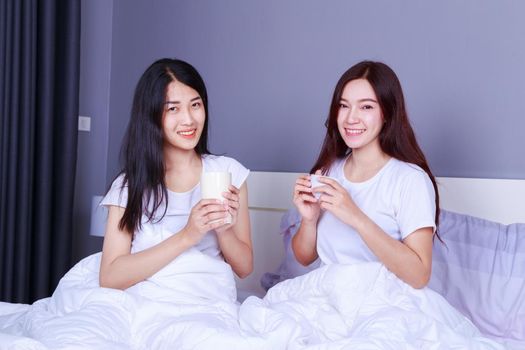 two best friends talking and drinking a cup of coffee on bed in the bedroom 