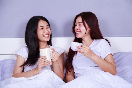 two best friends talking and drinking a cup of coffee on bed in the bedroom 