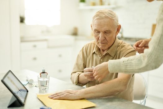 Serious elderly gentleman with a rolled-up sleeve receiving guidance about an injection