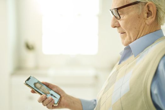 Cropped photo of an aged man in glasses holding a smartphone while consulting his physician via video call