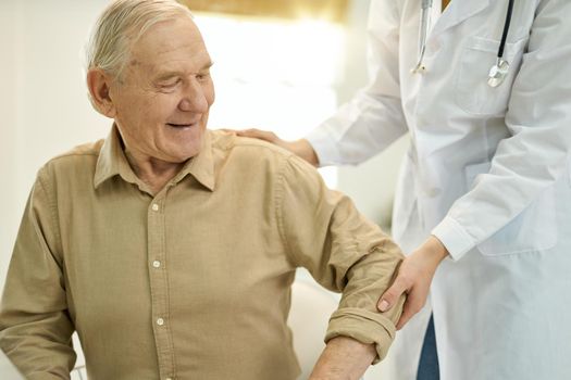 Fragment photo of healthcare worker in white lab coat helping a senior citizen get up from a chair