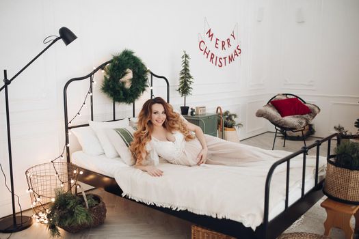 Beautiful smiling pregnant woman in white dress posing with New Year tree on background. Christmas and New Year concept