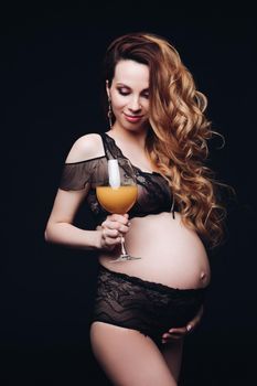 Waist up of happy pretty pregnant lady in black lingerie while posing in studio isolated on black background