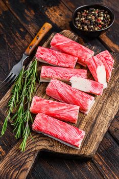 Sliced Crab surimi sticks on a wooden cutting board. Dark wooden background. Top view.