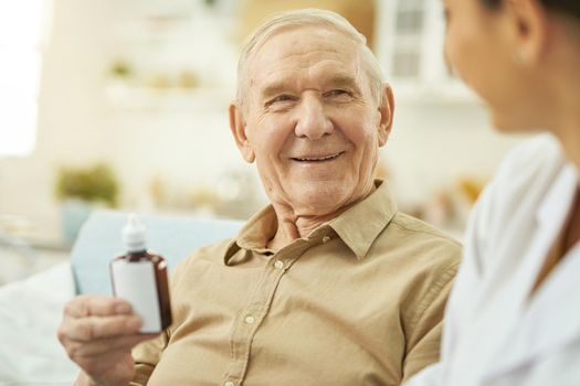 Smiling senior citizen looking at nurse and holding medicine while sitting at home