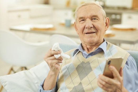 Old-aged man using smartphone, holding a handkerchief and consulting online. Copy space