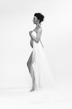 attractive caucasian pregnant female with dark hair posing to the camera only with a white cloth on her body