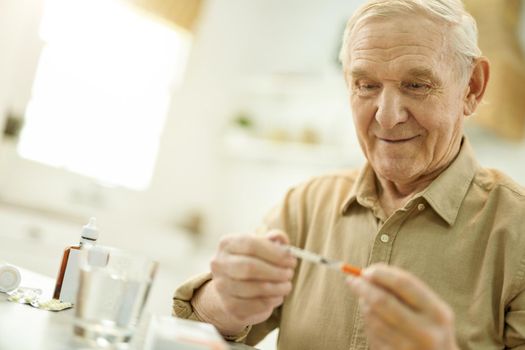 Copy-space photo of attentive senior gentleman looking at the thin syringe in his hands while staying home