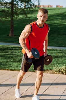 athletic man with dumbbells in his hands outdoors in the park. High quality photo