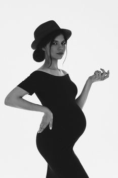 Beautiful pregnant young girl with tummy wearing hat and black dress expecting baby. Stylish pregnancy. Black and white. High quality photo