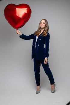 caucasian woman with attractive appearance holds a red air baloon, picture isolated on grey background