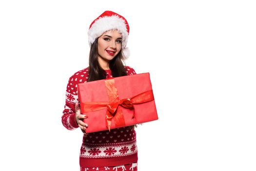 Young woman with long beautiful hair in Santa hat and New Year's dress holding Christmas present in her hands isolated on white background. Christmas sale. Emotional brunette. Copy space