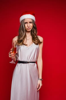 Portrait of upset young woman in santa hat posing in studio, isolated on red background. Party concept