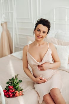 cheerful pregnant woman sits on the sofa with a boquet of beautiful flowers and touches her belly