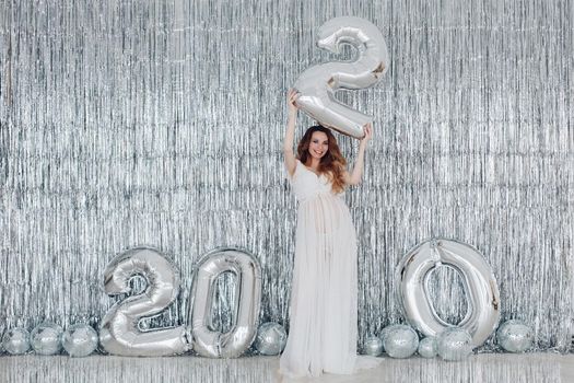 Beautiful smiling pregnant woman in white dress posing with New Year tree on background. Christmas and New Year concept