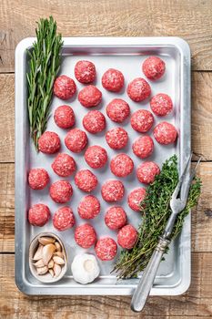 Recipe for cooking meatballs from ground beef with thyme and rosemary in kitchen tray. Wooden background. Top view.