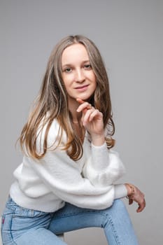 Pretty young female holding hand near the chin while looking at camera, isolated on grey background