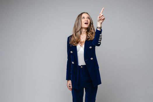 caucasian woman with attractive appearance points something her finger up, picture isolated on grey background