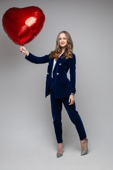 caucasian woman with attractive appearance holds a red air baloon, picture isolated on grey background