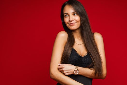 Studio portrait of attractive smiling woman with long straight brown hair in black top with lace design posing on red background. Copy space.