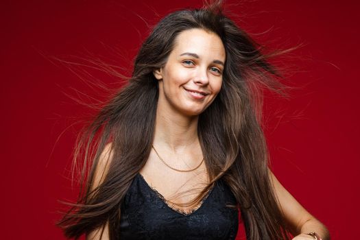 Head shot of long haired smiling brunette young joyful female with healthy hairs on red background with copy space. High quality photo