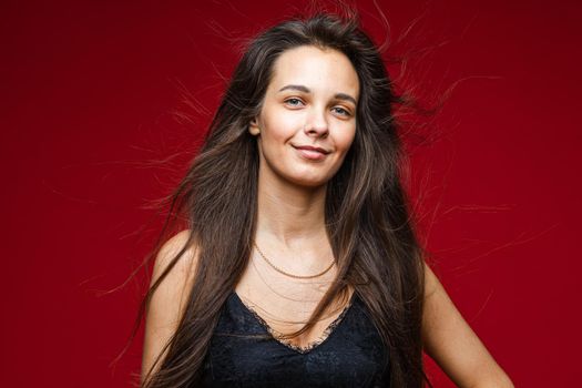 Head shot of long haired smiling brunette young joyful female with healthy hairs on red background with copy space. High quality photo