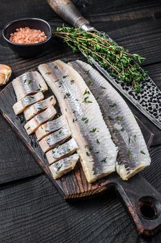Sliced salted herring fish fillet on a wooden board. Black wooden background. Top view.