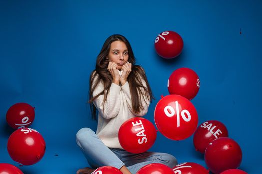 Smiling pretty lady holding two red balloons in studio, isolated on blue background. Shopping holiday concept