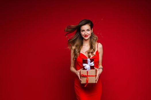 cheerful caucasian woman with attractive appearance with a lot of holiday gifts, picture isolated on red background