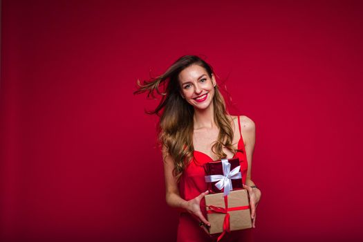 cheerful caucasian woman with attractive appearance with a lot of holiday gifts, picture isolated on red background